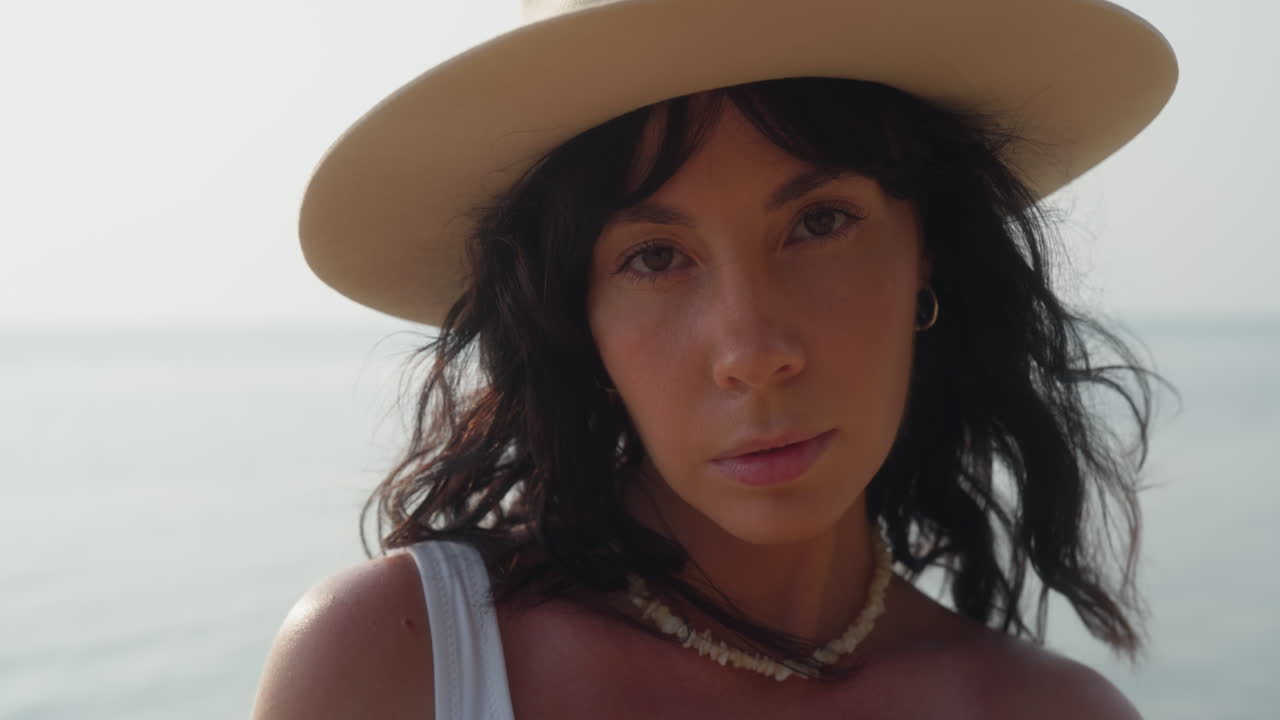 Ritratto in primo piano di una donna sicura di sé con un cappello in riva al mare