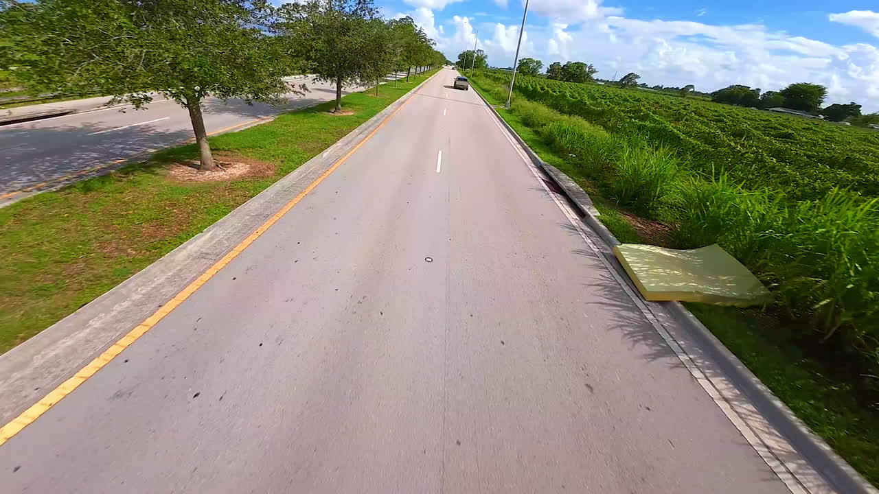 Following Tesla Cybertruck running by the asphalt highway along the lush greenery. FPV drone catching up with the futuristic car in the countryside on sunny day.