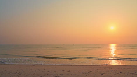 slowmo: golden sun reflects on turquoise ocean surface as waves hits pink sandy beach