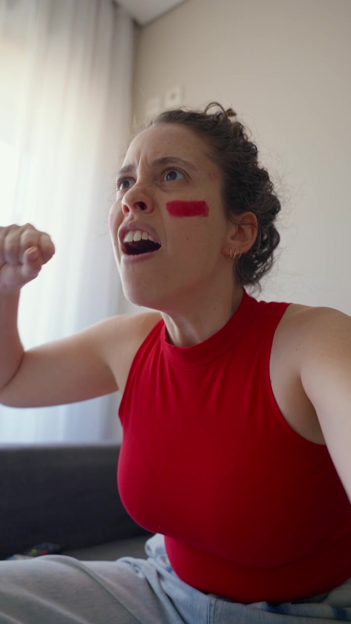 Young woman watching live sports game on TV angry and upset UGC POV style shot. Live streaming social media reel vertical phone camera as she gets mad disappointed by defeat result or negative score