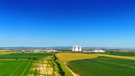 flight above the green countryside on sunny day. aerial perspective on the large factory producing white smoke