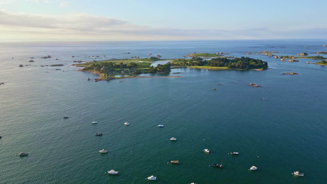 Panorama drone view of moored boats at Port Blanc scattered around small rocky islets with calm seawater, Côtes-d'Armor, Brittany, France.