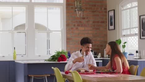 feliz pareja biracial que celebra el día de san valentín comiendo en casa