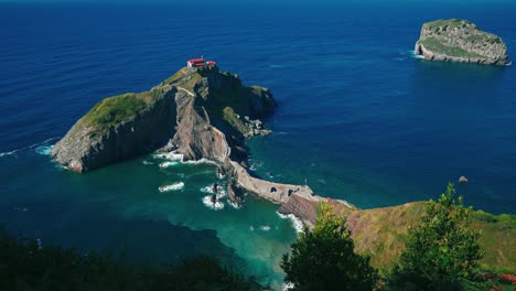 cinemagraph / seamless video loop of the famous game of thrones castle gaztelugatxe in the spanish basque country with a bridge across the seaside bay in northern spain with blue water and tourists on vacation exploring the scenic filming location.