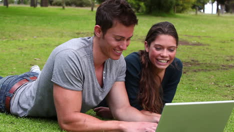 Two-friends-talking-to-each-other-as-they-use-a-laptop-while-lying-together