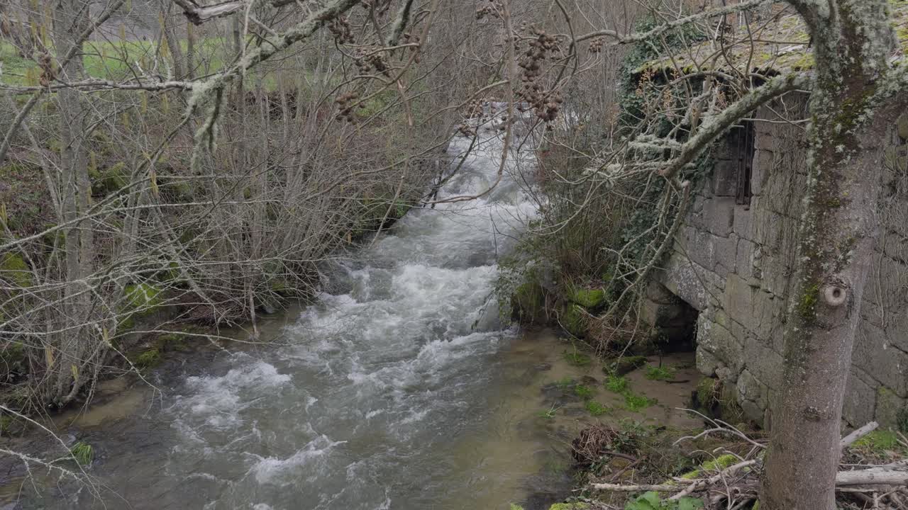 Fiume impetuoso accanto a un edificio in pietra abbandonato e cespugli