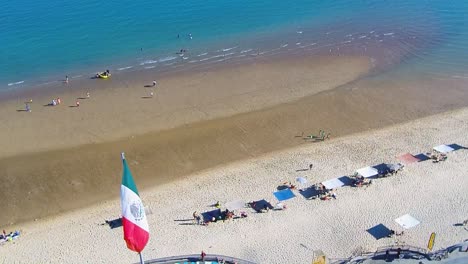 Blick-Auf-Eine-Zurückfliegende-Drohne,-Die-Einen-Strand-Und-Die-Mexikanische-Flagge-Zeigt