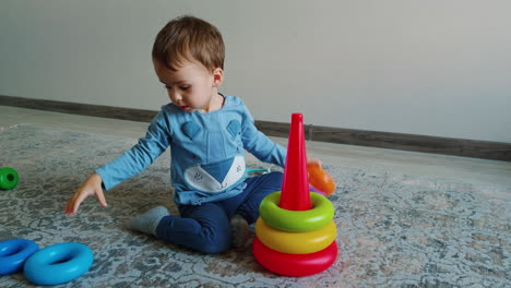lovely baby boy plays with toy pyramid at home. toddler studies shapes, sizes and colors.