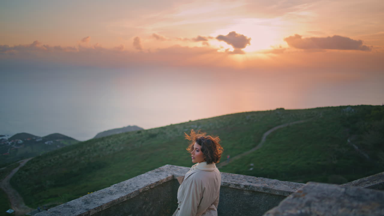 Nachdenkliche Frau, die den Sonnenuntergang am Horizont betrachtet und sich an ein Geländer lehnt. Reisende Frau.