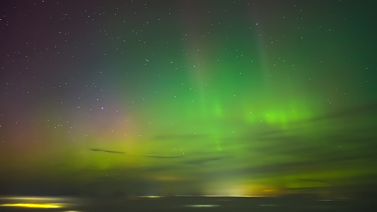 Timelapse di una vibrante aurora boreale che danza su un mare ghiacciato sotto cieli stellati, con un bagliore verde e rosa all'orizzonte.