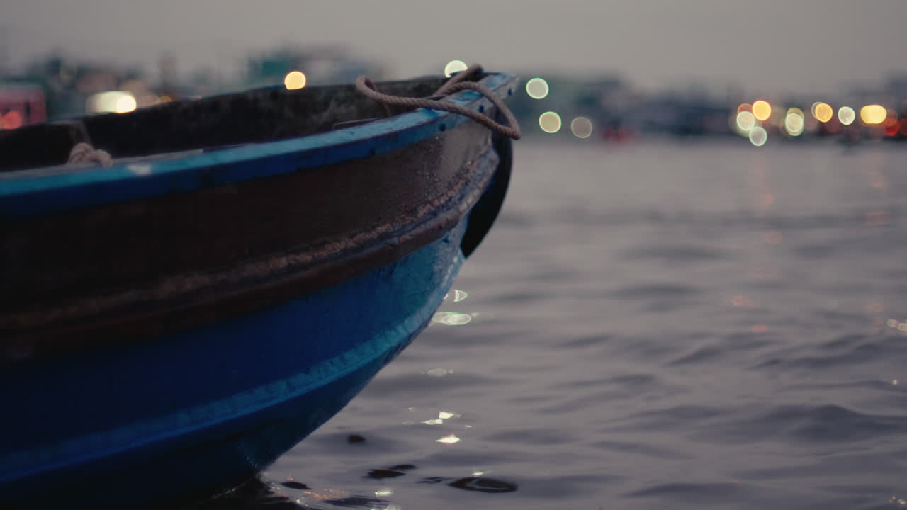 A boat resting on calm water with a beautiful bokeh cityscape backdrop at dusk in Vietnam
