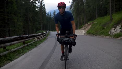 Healthy-Male-cycling-behind-a-car-at-high-speed-in-the-mountains-in-the-Italian-Dolomites-in-Italy,-Europe