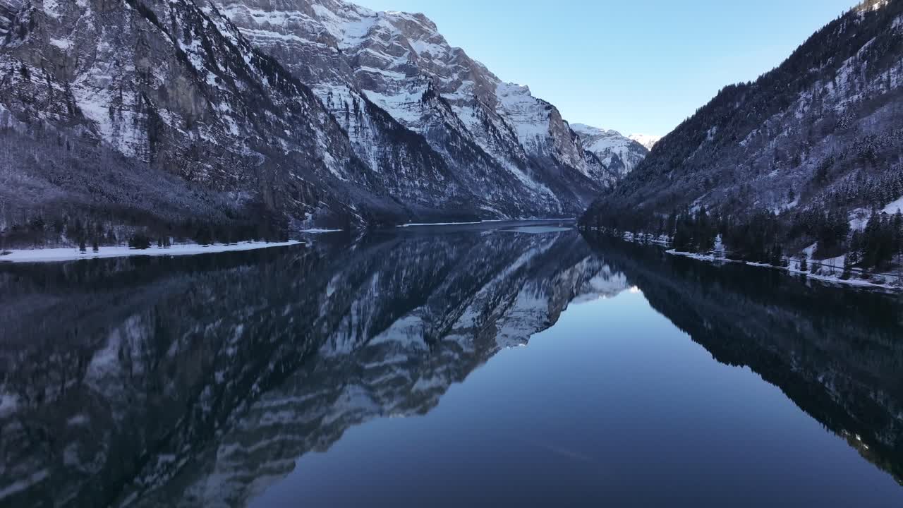 A calm alpine lake reflects snow-covered mountains in Klöntal, Glarus, Switzerland