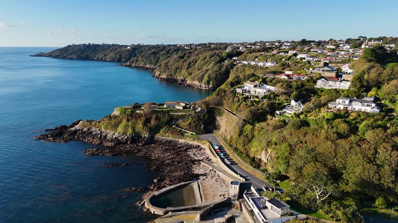High distant drone footage along coastline of Havelet Bay Guernsey seawater bathing pools,Fort George Clarence Battery views along coast and across the Island on calm day in late afternoon sunshine