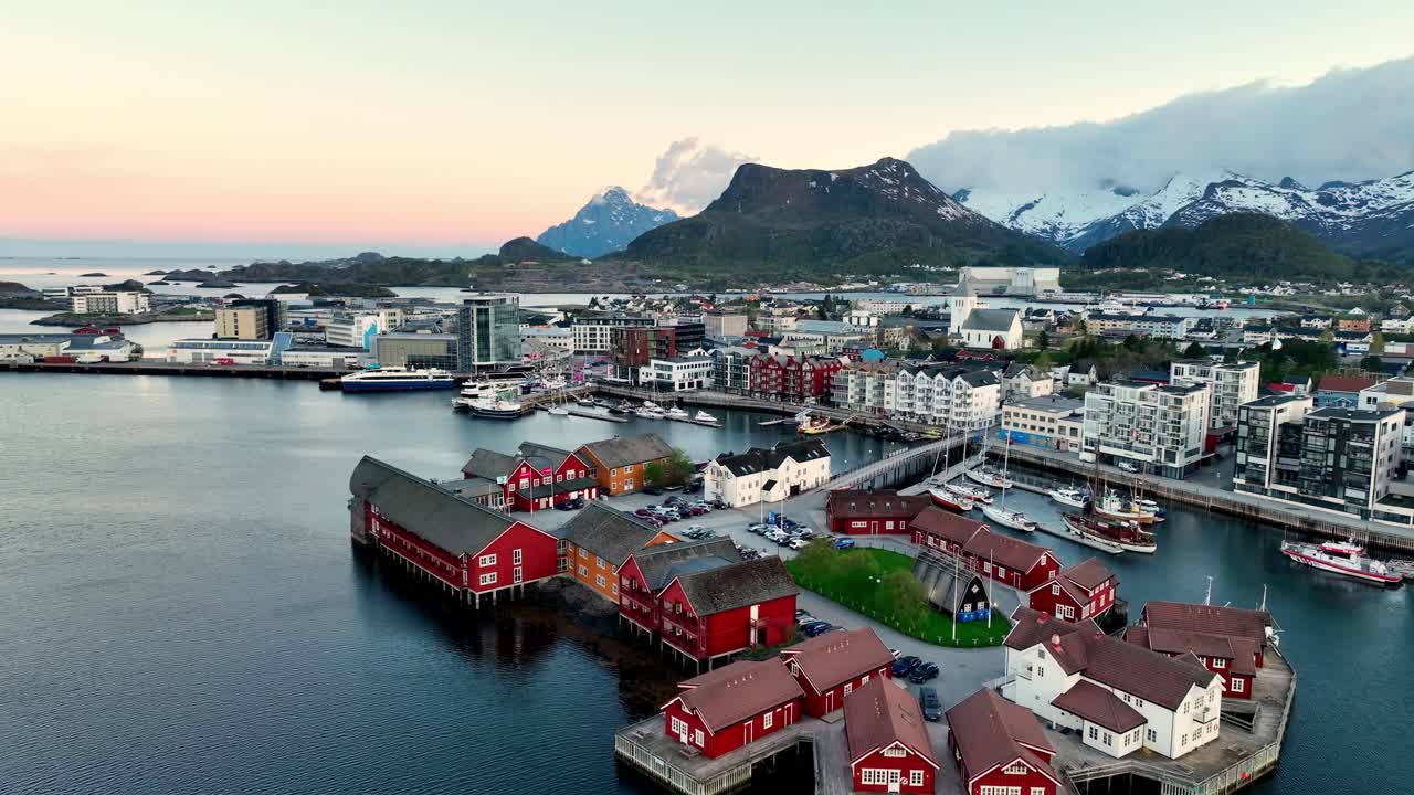 Drone flies toward Lamholmen in Svolvaer showing city, harbor and mountains under midnight sun