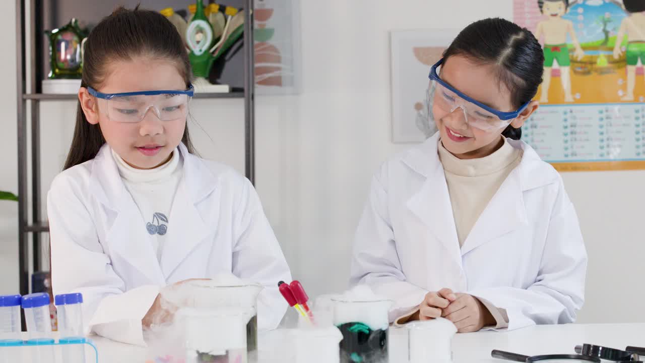 白衣を着た2人の幼いアジア人の女の子が、煙の出るビーカーを使って化学実験を行っている
