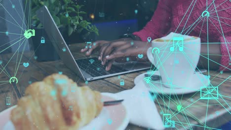animación de iconos de medios conectados sobre una mujer afroamericana que usa una computadora portátil en un café