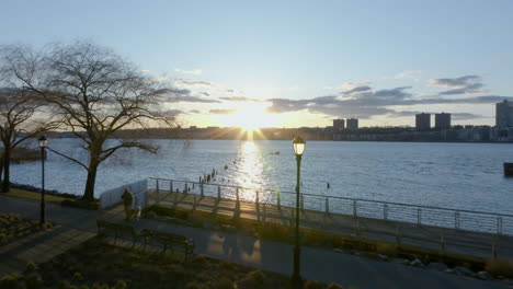 People-riding-bikes-and-walking-on-the-coast-of-the-Hudson-river,-sunrise-in-New-York---Aerial-view