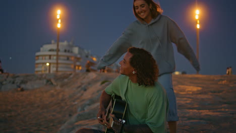 pareja tocando la guitarra en la playa por la noche