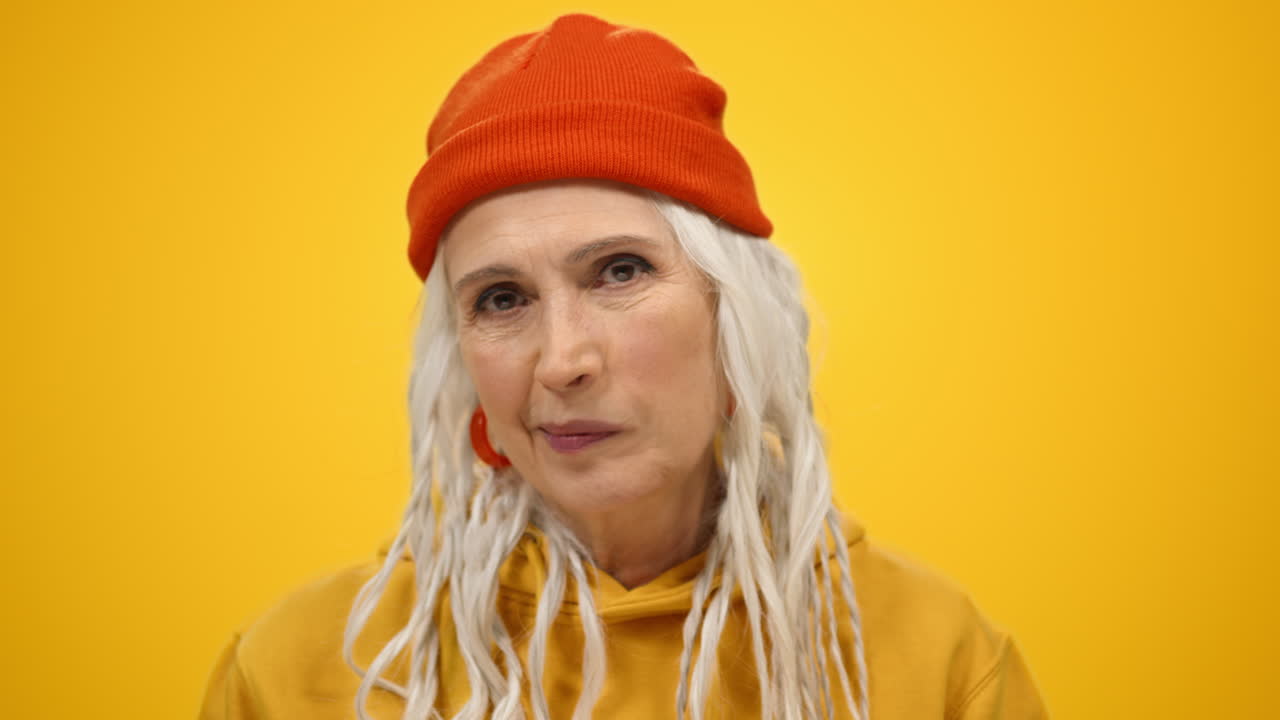 혼란스러운 시니어 여성이 실내에서 눈을 돌리고 지루한 여성이 스튜디오에서 미소를 짓고 있습니다.