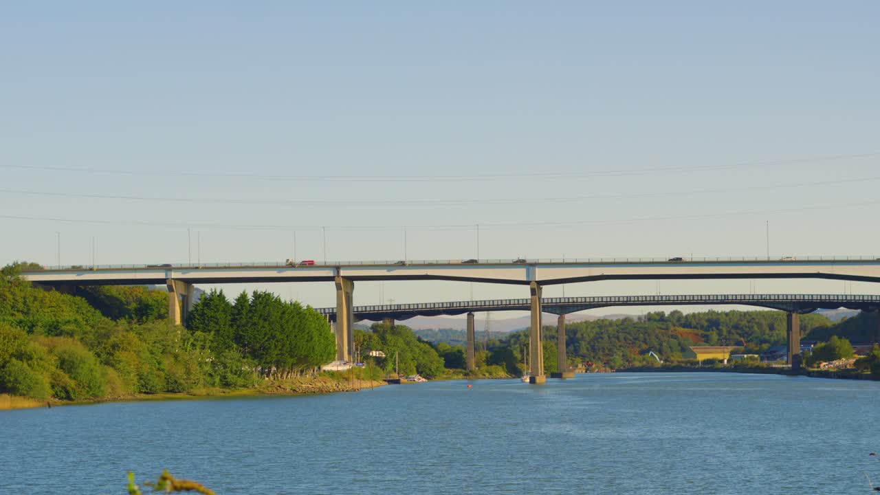 Pan Across M4 Motorway Overpass Bridge with Steady Traffic Travelling Between Port Talbot and Swansea. River Neath at High Tide with Trees. Commuters in Cars Surrounded by Nature