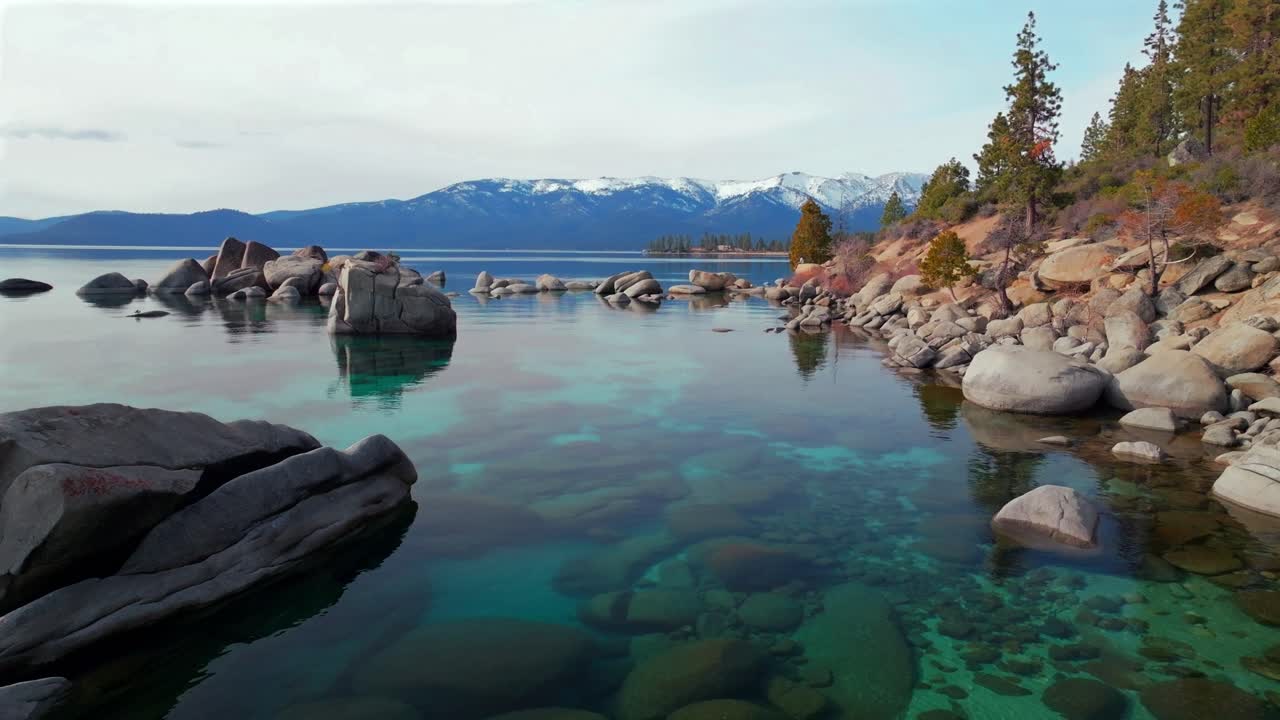 Lake Tahoe standing on rocky large boulders shoreline clear glassy turquoise fresh water aerial drone Sand Harbor California sunny winter clouds Secret Chimney beach Incline Village Kings Beach static