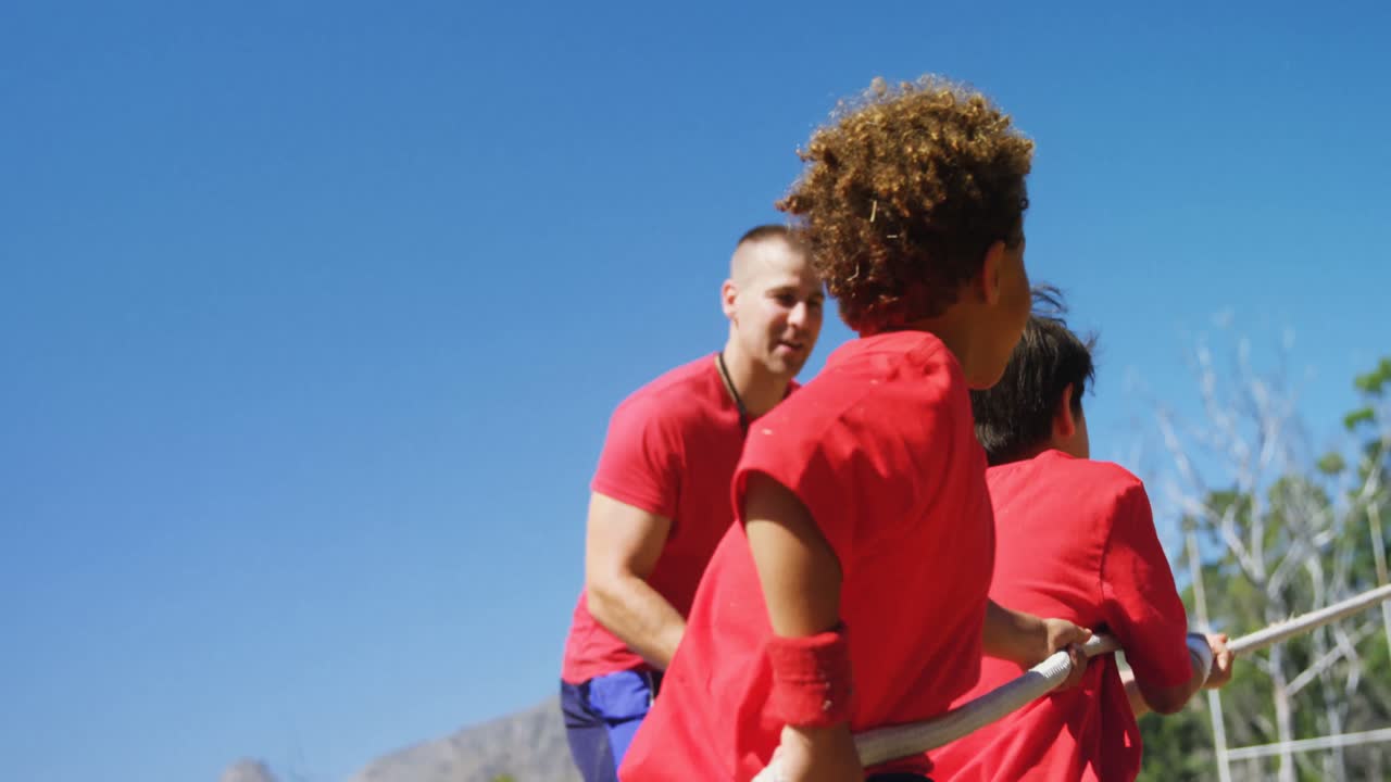 entrenador ayudando a los niños en el tira y afloja durante el entrenamiento de cursos de obstáculos