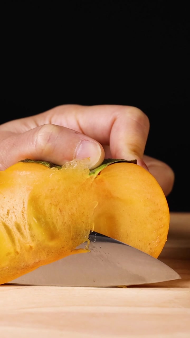 Una mano usa un coltello da chef per affettare un cachi fresco arancione su legno