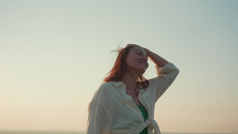 sunlit young woman spinning joyfully on hilltop under warm sky overlooking river valley as breeze lifts hair in golden evening light silhouette dancing with nature in calm serene moment of freedom