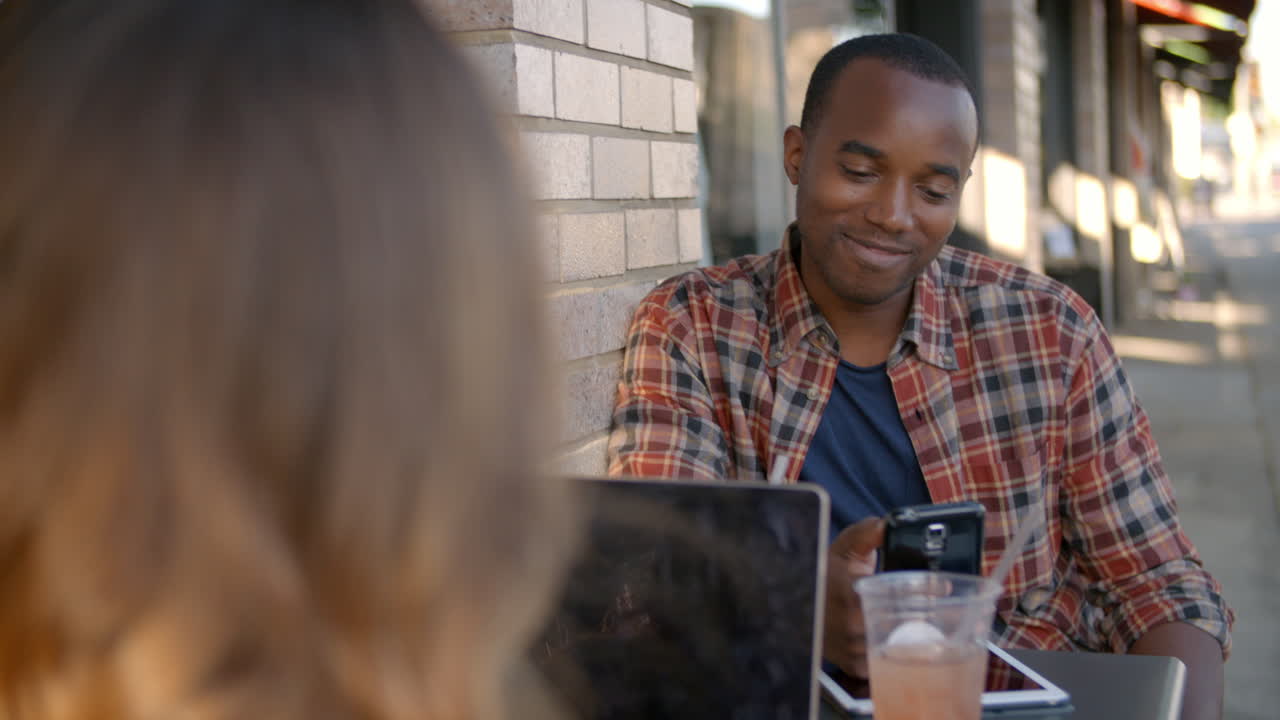 Mixed race couple using technology outside a coffee shop