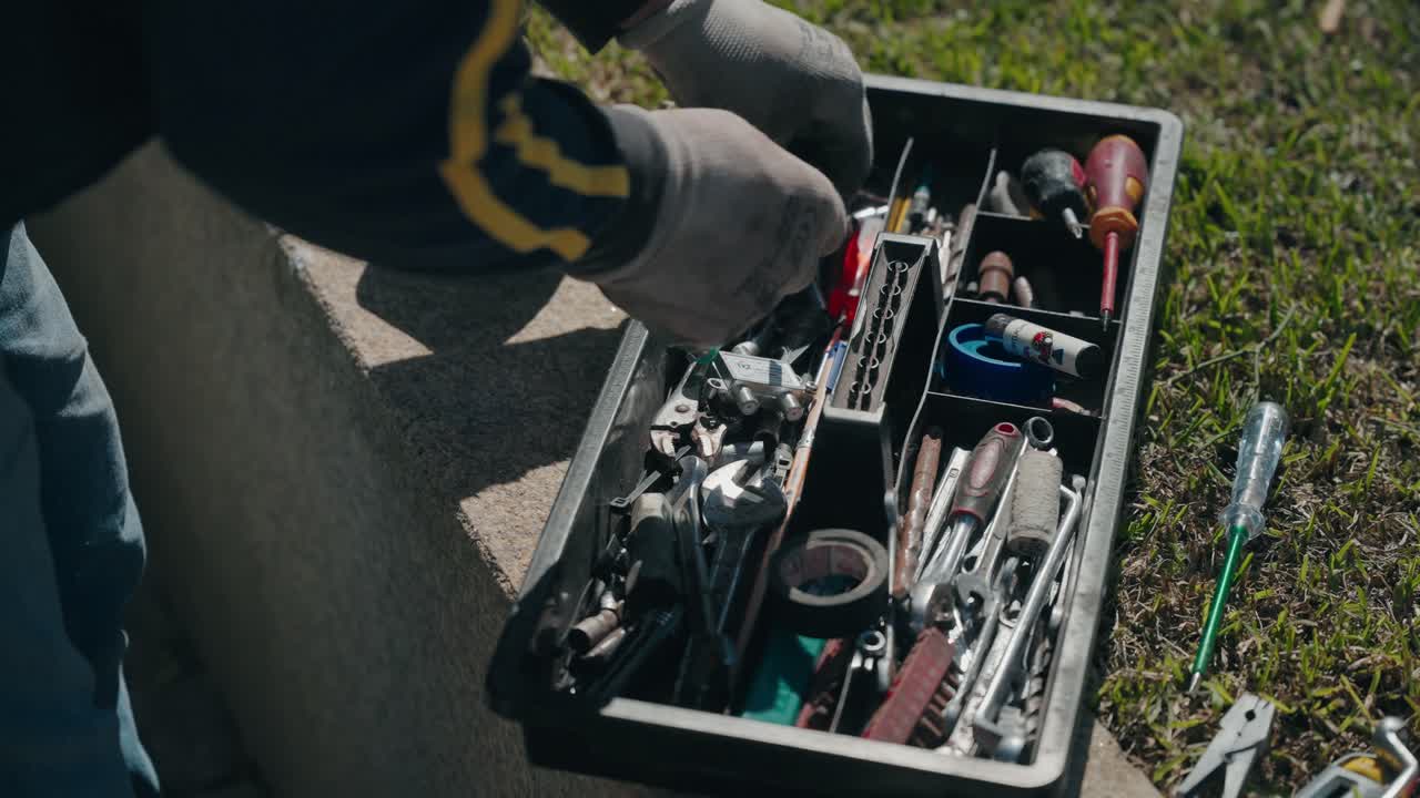 Open toolbox filled with assorted hand tools placed on ground outdoors