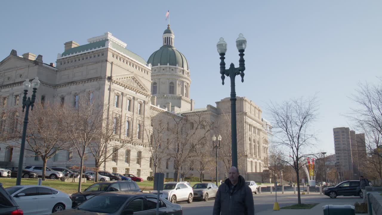 fuera del edificio del capitolio del estado de indiana en indianapolis, indiana con un hombre caminando por la acera con video estable