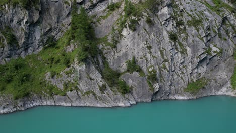 Profilansicht-Eines-Vollständig-Felsigen-Hügels-Mit-Flecken-Grünen-Geländes,-Zerbrochenen-Steinen-Des-Berges-An-Den-Rändern,-Bäumen,-Die-Am-Ufer-Wachsen,-Tiefblaues-Wasser,-Das-Sich-Seitwärts-Bewegt,-Filmischer-Naturdokumentationsstil