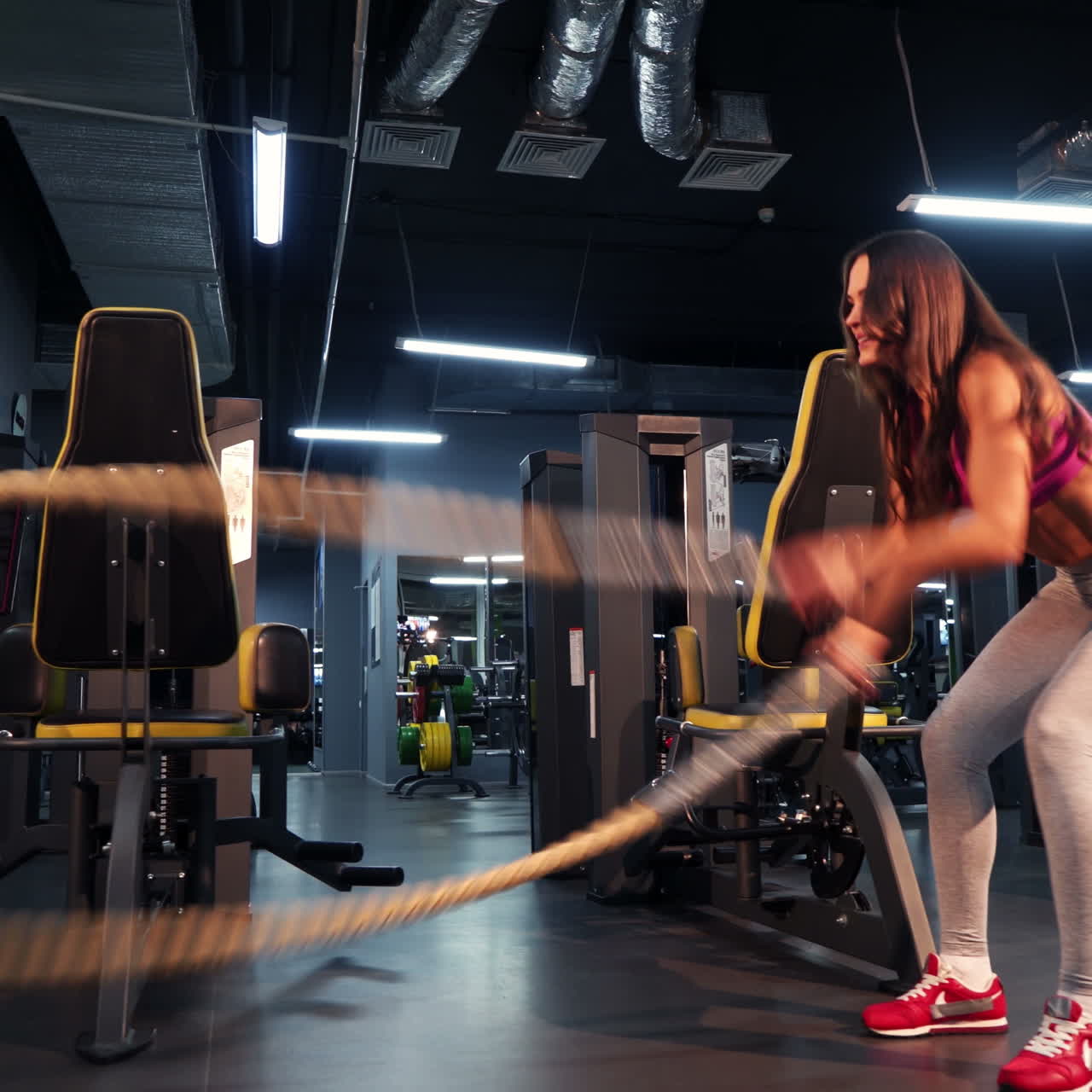 Muscular fitness woman trains triceps with two cables by her hands on the background of a new fitness center. Fit woman exercise with cable crossover in gym.