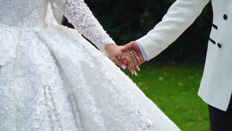 freshly married couple bride and groom are waling together through park nature holding hands smart clothes celebration event olive skin cinematic close up