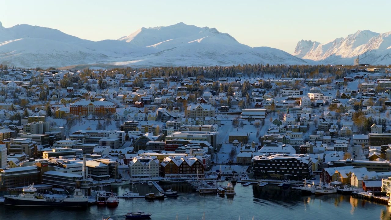 Schneebedeckte Stadtlandschaft von Tromsø, umgeben von verschneiten Bergen im Winter. Luftaufnahme.