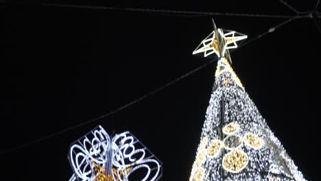giant christmas tree glittering in white and gold string lights standing beside the hanging bell-shaped lantern - close-up shot