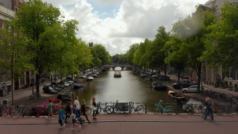 Amsterdam-Canal-Bridge-with-a-Group-of-Tourists-wearing-Masks,-Cityscape-Crane-Aerial