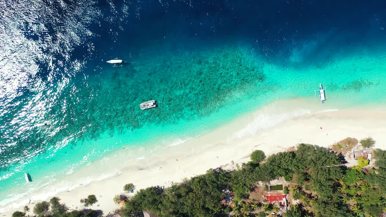 Spiaggia bianca e sabbiosa di un'isola tropicale bagnata da una laguna turchese che riflette la luce del sole, barche che galleggiano sulla costa a Turks e Caicos