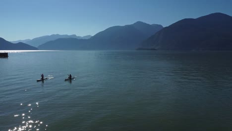 two kayakers paddling back to shore in the ocean of porto cove, bc