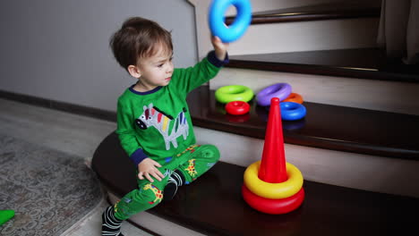 toddler boy sits on the stairs building a pyramid. cute child playing games at home.