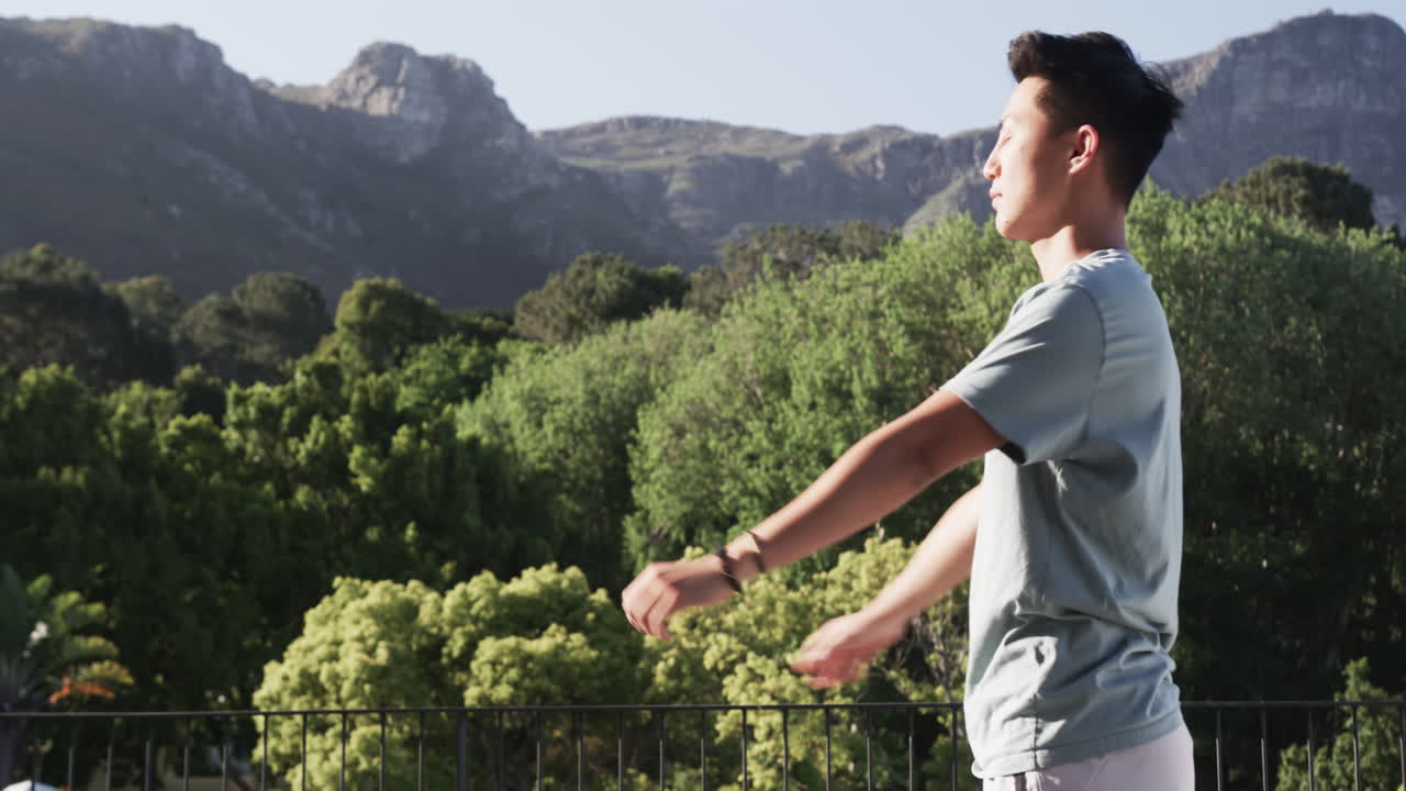 Asian man practicing Tai Chi outdoors with scenic mountain view, on balcony, copy space