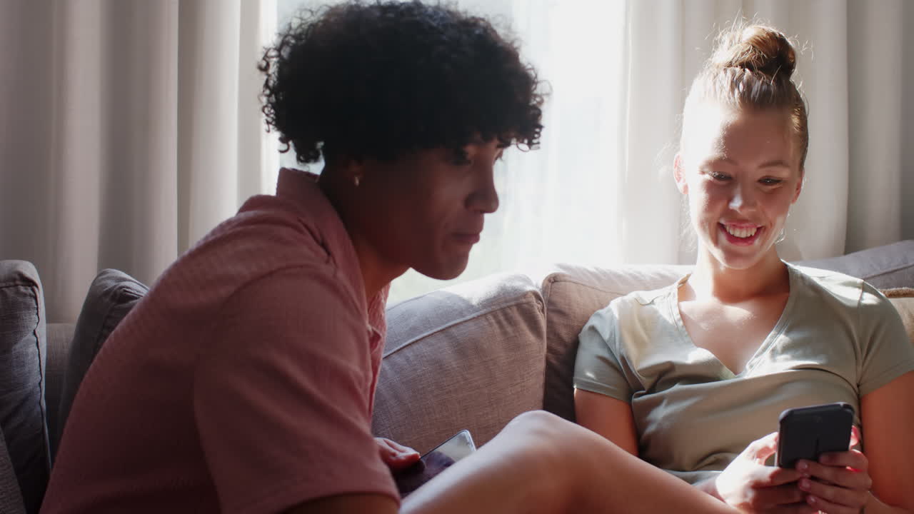 Smiling woman holding coffee cup and smartphone, enjoying conversation on sofa, at home, copy space