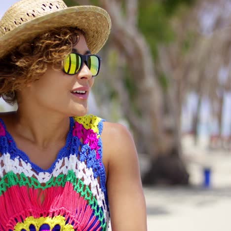 mujer sonriente con gafas de sol y sombrero cerca del océano