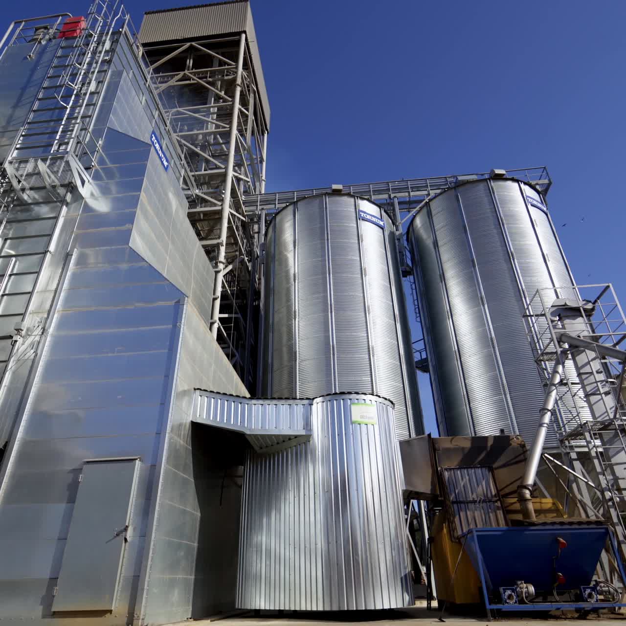 New metal construction of grain elevators. Huge agricultural plant in the countryside. Silver silos for storing crop in bright sunny day.
