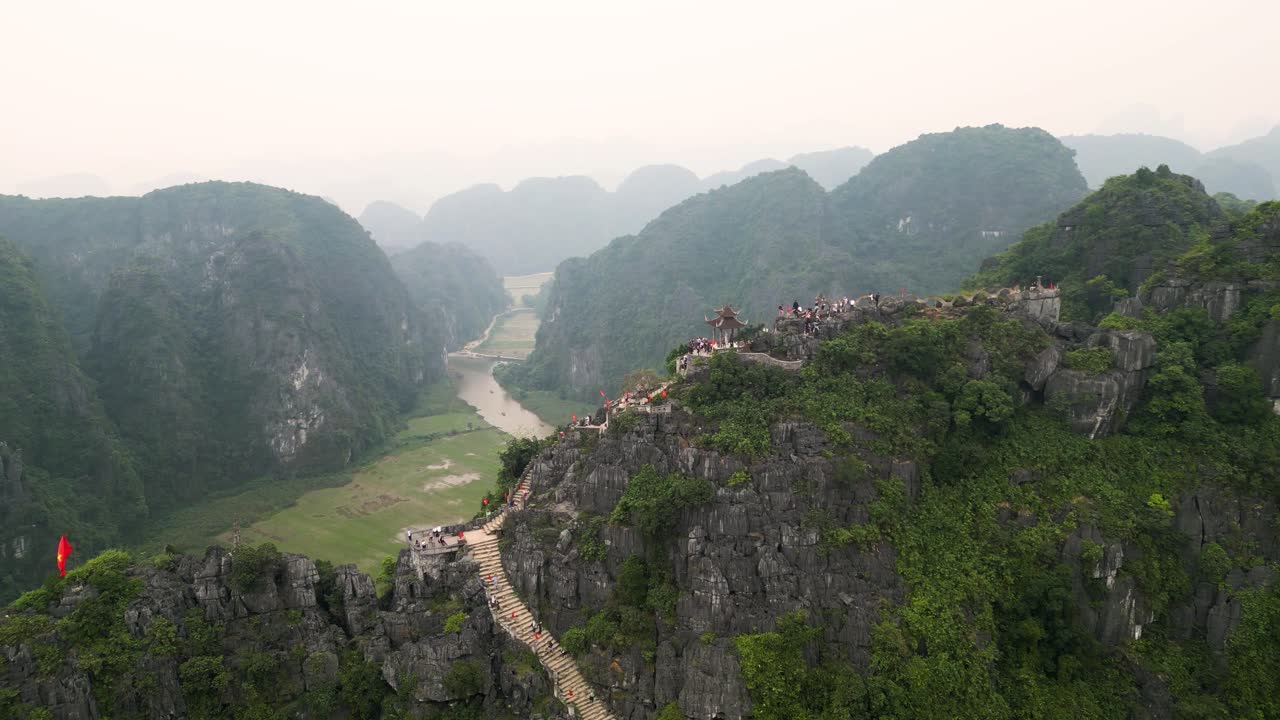 Tourists Climb On The Hang Mua Viewpoint Overlooking The Caves, River And Mountains In Tam Coc, Vietnam. - aerial shot