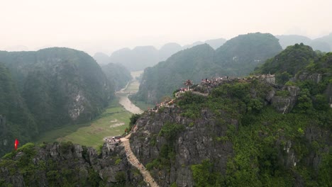 tourists climb on the hang mua viewpoint overlooking the caves, river and mountains in tam coc, vietnam. - aerial shot
