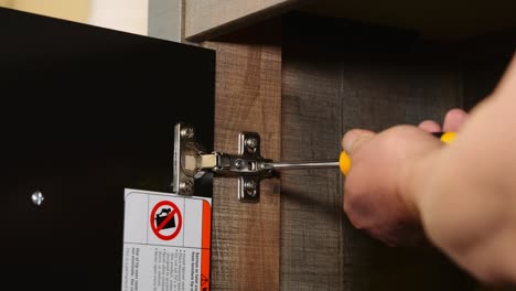 un carpintero de reparación de muebles utiliza un destornillador de cabeza philips para ajustar los tornillos en una bisagra de gabinete ajustable europea