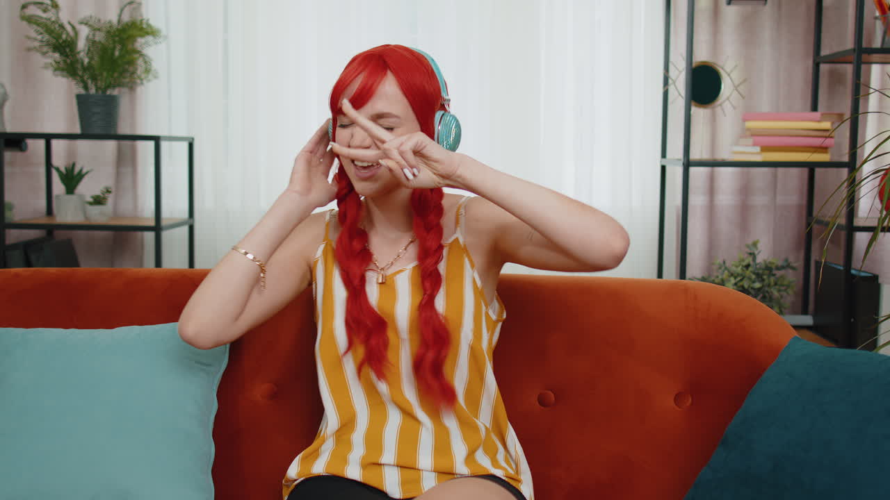 chica pelirroja feliz con auriculares inalámbricos bailando escuchando su música rock n roll favorita en el sofá de casa
