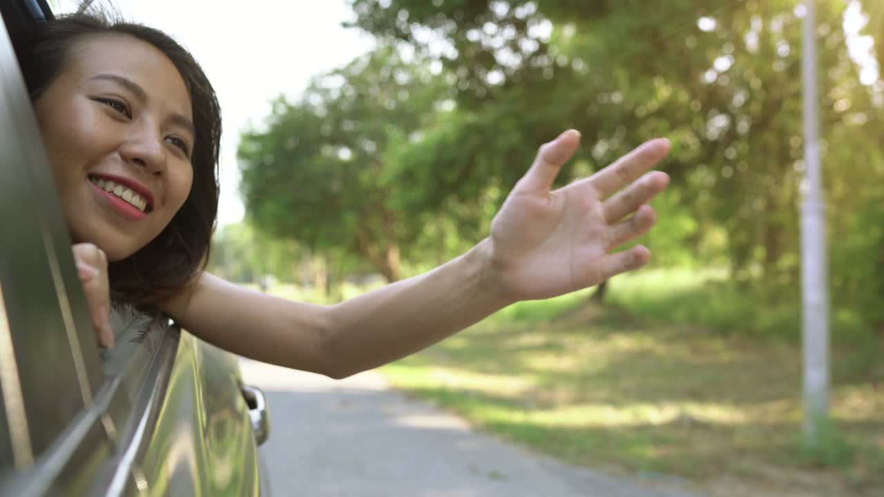 젊은 아시아 여성이 자동차 창문으로 바람을 느끼는 것을 즐기고 있습니다.